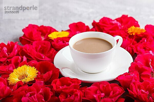 Rote Rosenblüten und eine Tasse Kaffee auf einem grauen Betonhintergrund. Morninig  Frühling  Mode Zusammensetzung. Seitenansicht  selektiver Fokus  Nahaufnahme
