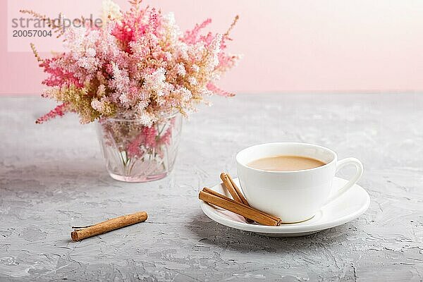 Rosa und rote Astilbe Blumen im Glas und eine Tasse Kaffee auf einem grauen und rosa Hintergrund. Morninig  Frühling  Mode Zusammensetzung. Seitenansicht  Nahaufnahme  selektiver Fokus