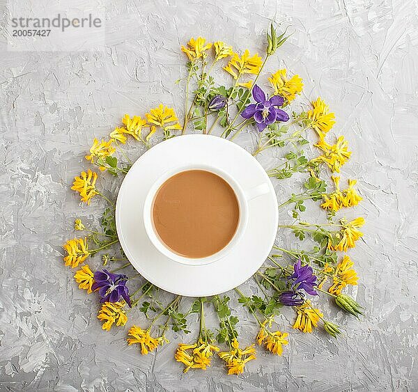 Gelbe und blaue Blumen in einer Spirale und eine Tasse Kaffee auf einem grauen Hintergrund aus Beton. Morninig  Frühling  Mode Zusammensetzung. Flachlage  Draufsicht  Nahaufnahme