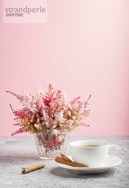 Rosa und rote Astilbe Blumen im Glas und eine Tasse Kaffee auf einem grauen und rosa Hintergrund. Morninig  Frühling  Mode Zusammensetzung. Seitenansicht  Nahaufnahme  selektiver Fokus