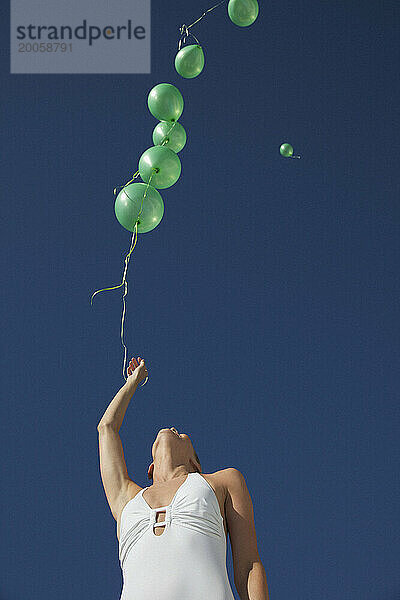 Frau lässt grüne Luftballons in einem wolkenlosen Himmel los – Blick aus der Tiefe