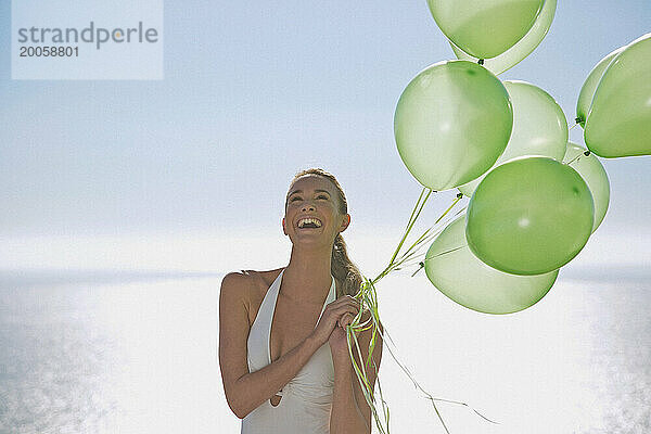 Nahaufnahme einer Frau  die lächelnd ein Bündel grüner Luftballons hält