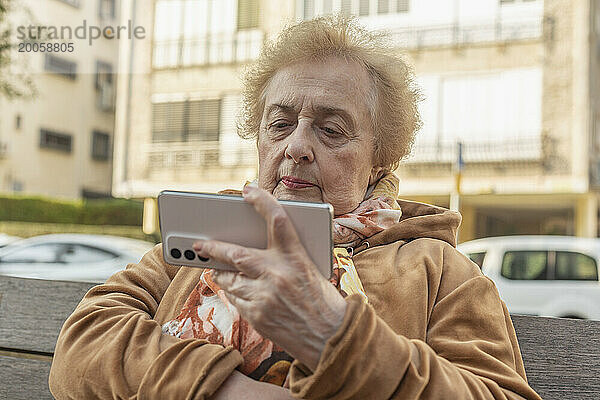 Ältere Frau sitzt und benutzt Smartphone auf Stadtbank