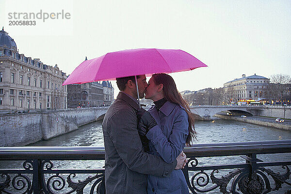 Paar küsst sich unter einem rosa Regenschirm auf einer Brücke über die Seine  Paris  Frankreich