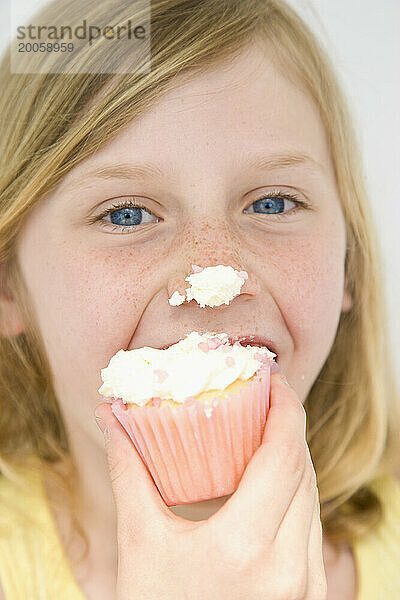 Junges Mädchen beißt Cupcake mit Zuckerguss auf der Nase