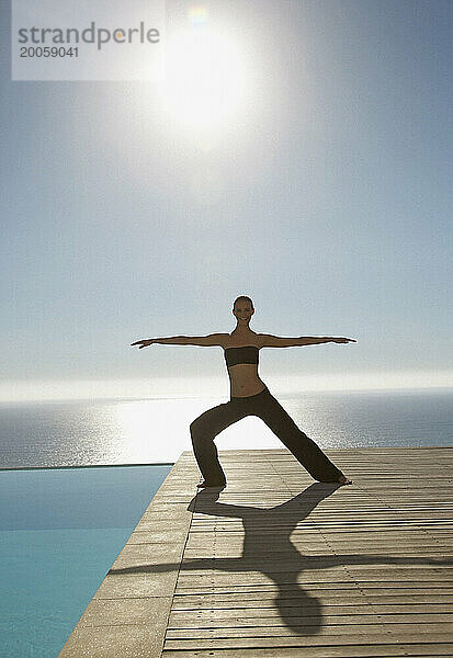 Junge Frau praktiziert Yoga an einem Swimmingpool mit Meer im Hintergrund