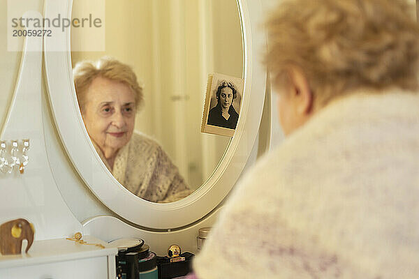 Lächelnde ältere Frau blickt auf das Spiegelbild neben einem alten Foto