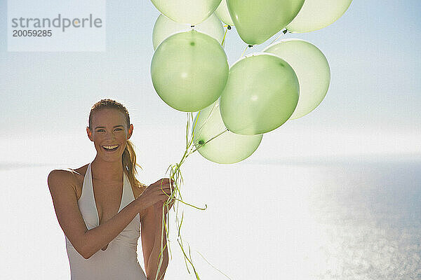 Nahaufnahme einer Frau  die lächelnd ein Bündel grüner Luftballons hält