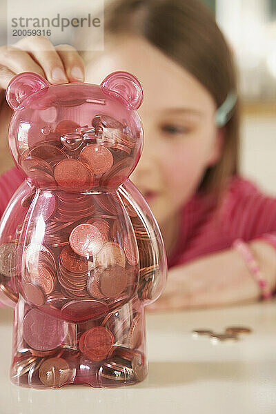 Mädchen steckt Münzen in eine Spardose in Form eines Teddybären