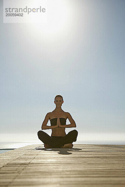 Junge Frau praktiziert Yoga an einem Swimmingpool mit Meer im Hintergrund