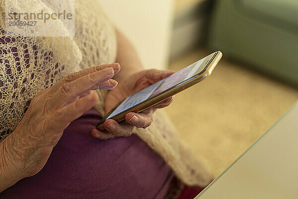 Nahaufnahme der Hände einer älteren Frau  die ihr Smartphone benutzt