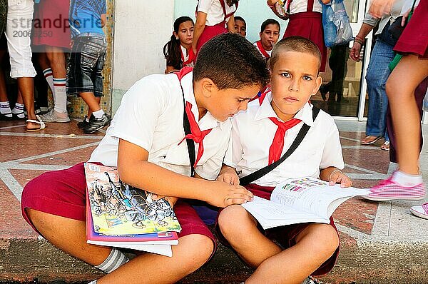 Zwei kubanische Schuljungs in Cienfuegos auf dem Gehsteig sitzend und Aufgaben machend. Zwei kubanische Schuljungen lernen sitzend auf dem Gehsteig