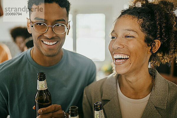 Fröhlicher junger Mann und Frau mit Bierflaschen in der Küche