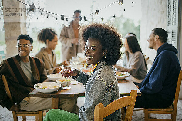 Porträt einer glücklichen Frau mit Afro-Frisur  die während einer Dinnerparty auf der Terrasse ein Weinglas hält