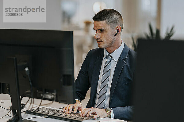 Selbstbewusster junger Geschäftsmann tippt  während er am Schreibtisch im Büro den Computer benutzt