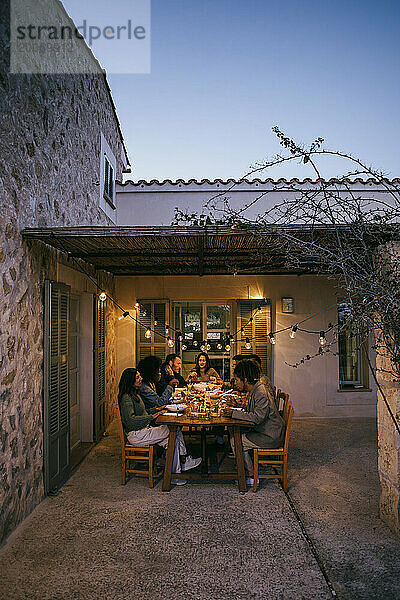 Gemischtrassige Freunde sitzen während der Dinnerparty am Esstisch auf der Terrasse