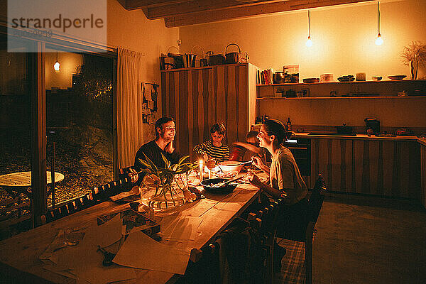 Glückliche Familie genießt ein Abendessen bei Kerzenschein  während sie zu Hause am Esstisch sitzt