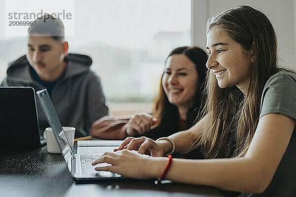 Lächelndes Mädchen mit Laptop von Mutter und Bruder am Esstisch