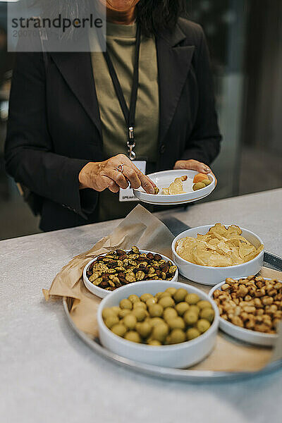 Mittelteil einer leitenden Geschäftsfrau  die während einer Networking-Veranstaltung Snacks auf dem Teller isst