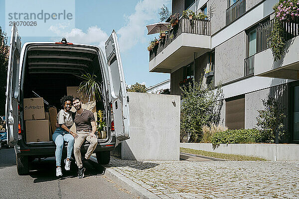 Gemischtrassiges Paar sitzt im Kofferraum eines Lieferwagens in der Nähe eines Gebäudes