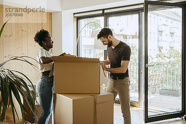 Glückliches gemischtrassiges Paar packt Kisten aus  während es im neuen Zuhause steht