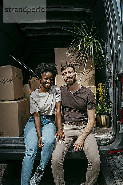 Porträt eines glücklichen Freundes und einer glücklichen Freundin  die zusammen im Kofferraum eines Lieferwagens mit Kisten sitzen