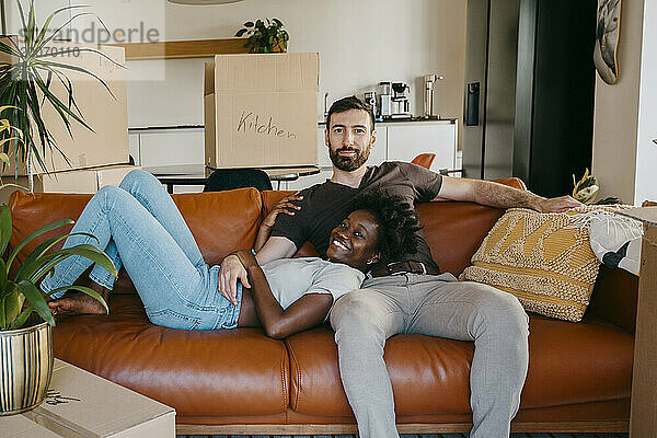 Porträt eines gemischtrassigen Paares  das es sich auf dem Sofa im Wohnzimmer im neuen Zuhause gemütlich macht