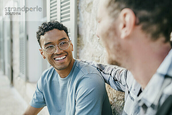 Lächelnde männliche Freunde reden  während sie im Hinterhof sitzen