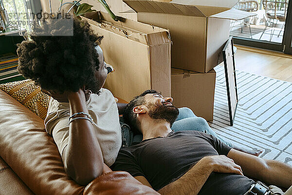 Gemischtrassiges Paar entspannt sich gemeinsam auf dem Sofa im Wohnzimmer im neuen Zuhause