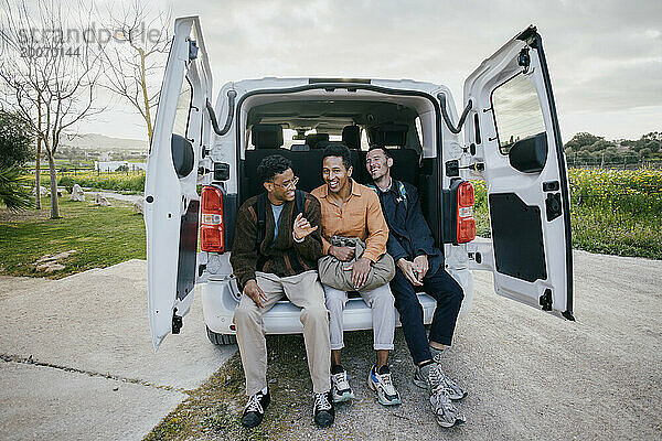 In voller Länge fröhliche männliche Freunde  die im Kofferraum eines Lieferwagens am Straßenrand sitzen