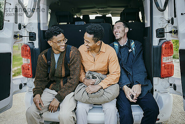 Fröhliche männliche Freunde sitzen im Kofferraum eines Lieferwagens
