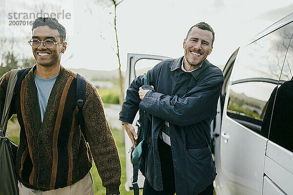 Lächelnde männliche Freunde mit Rucksäcken  die mit dem Van vorbeigehen