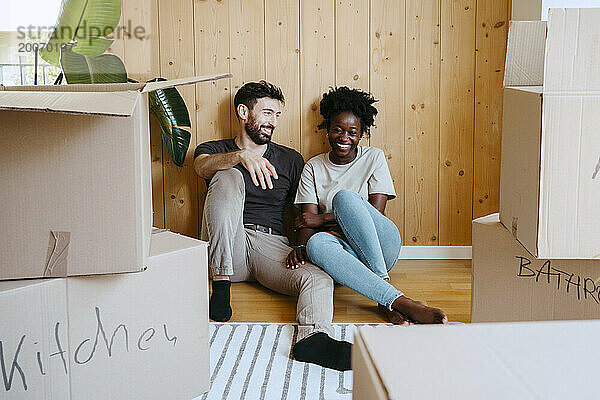 Glückliches gemischtrassiges Paar  das zusammen an einer Holzwand im neuen Zuhause sitzt