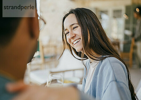 Lächelnde junge Frau im Gespräch mit einem Mann  der auf der Terrasse sitzt