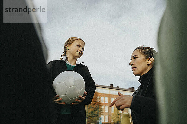 Trainerin gibt Grundschulmädchen mit Sportball gegen den Himmel Ratschläge