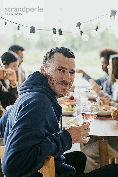 Porträt eines lächelnden reifen Mannes  der bei einer Dinnerparty auf der Terrasse mit Weinglas sitzt