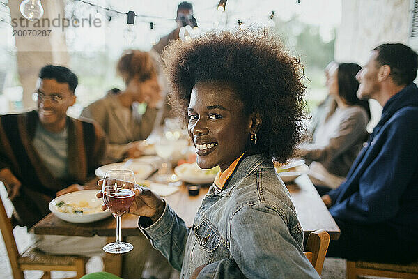 Lächelndes Porträt einer jungen Frau mit Afro-Frisur  die ein Weinglas hält