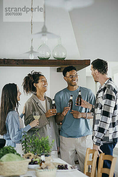 Fröhliche Freunde halten alkoholische Getränke in der Hand  während sie sich während der Dinnerparty zu Hause unterhalten