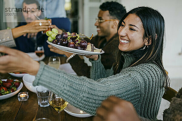 Lächelnde Frau hält während der Dinnerparty einen Obstteller auf der Terrasse