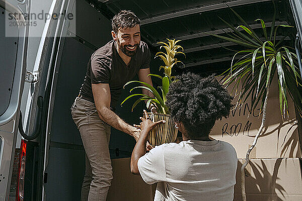 Lächelnder Freund übergibt Pflanze an gemischtrassige Freundin in der Nähe des Kofferraums eines Lieferwagens