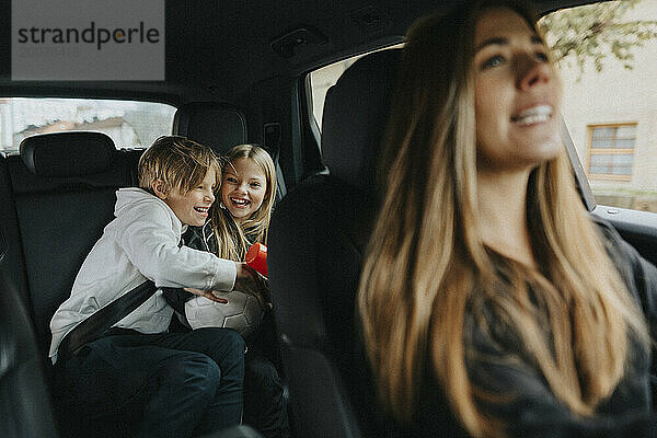 Glücklicher Bruder und Schwestern  die hinten sitzen  während Mutter am Wochenende Auto fährt