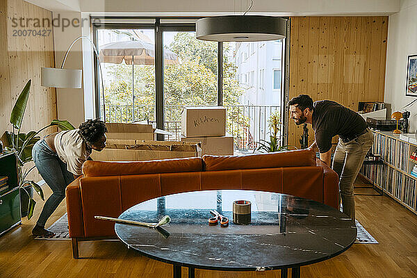 Gemischtrassiges Paar hilft sich gegenseitig  während es das Sofa im Wohnzimmer des neuen Zuhauses behält