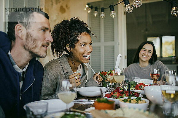 Lächelnde Frau sitzt mit Freunden am Esstisch zur Dinnerparty