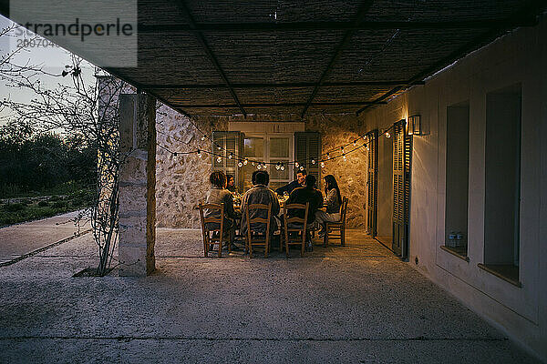 Männliche und weibliche Freunde sitzen während der Dinnerparty am Esstisch auf der Terrasse