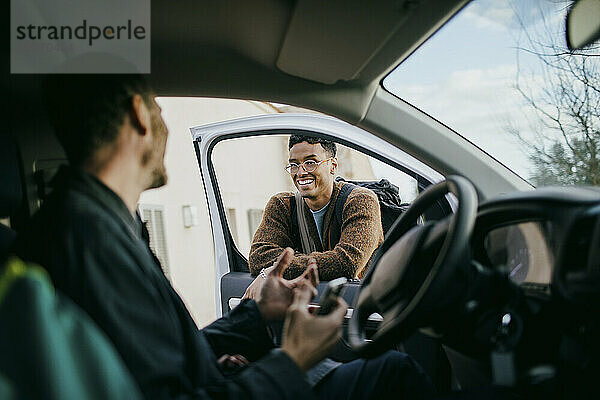 Lächelnder Mann schaut Freund an  der im Lieferwagen sitzt