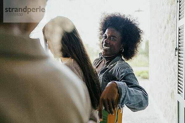 Glückliche Frau mit Afro-Frisur sitzt neben Freundinnen auf der Terrasse