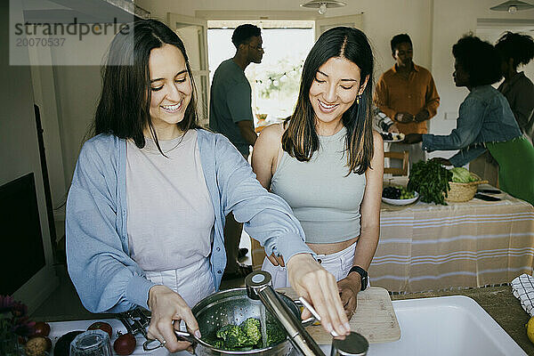 Glückliche Freundinnen bereiten gemeinsam in der Küche zu Hause das Abendessen zu