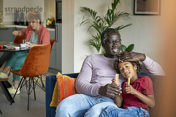 Familie gemischter Abstammung sitzt entspannt zu Hause. Kinder und Vater auf dem Sofa
