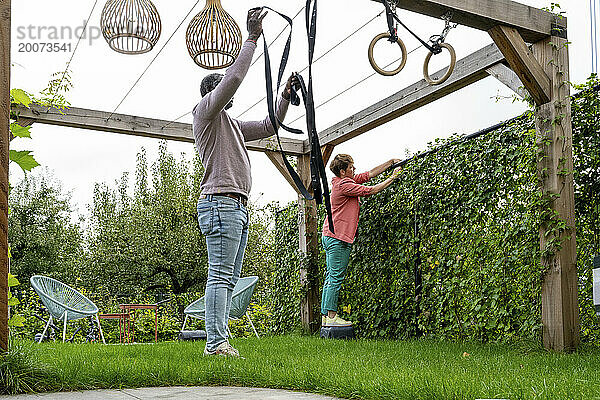 Eltern gemischter Abstammung putzen den Garten und stellen Sportgeräte auf  um fit zu bleiben