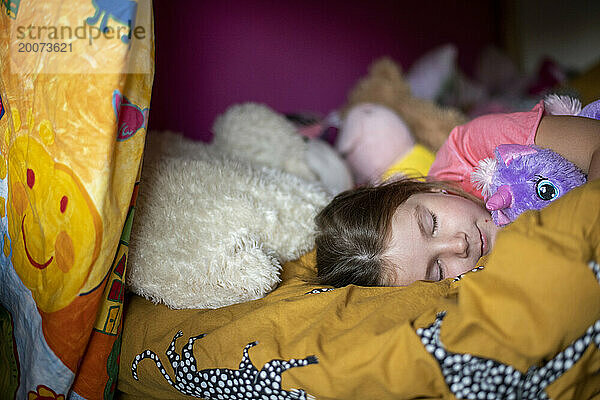 Junges Mädchen schläft friedlich auf ihrem Bett  umgeben von Teddys
